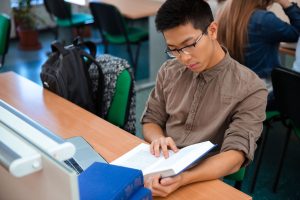 Portrait of a male student reading book in classroom